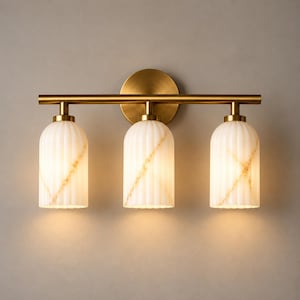 May include: A three-light wall fixture featuring a horizontal brushed brass bar and a circular wall mount. Three cylindrical, vertically ribbed white glass shades with subtle gold-toned veining hang from the bar, emitting a warm glow.