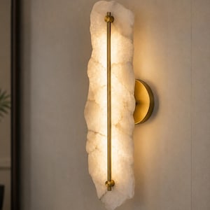 May include: A vertical wall sconce featuring a rough-hewn, translucent white stone slab illuminated from behind. A slender, brushed brass metal rod runs vertically down the center of the stone, secured by circular brass hardware at each end.
