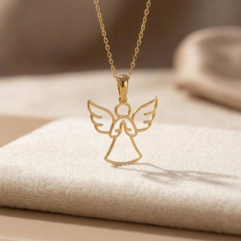 A shiny, outline-style angel pendant with outstretched wings and hands clasped in prayer, suspended from a delicate cable chain. The pendant is available in both a warm gold-tone finish and a bright silver-tone finish, reflecting light beautifully. This guardian angel necklace is a minimalist sterling silver angel design, suitable as a spiritual protection charm.