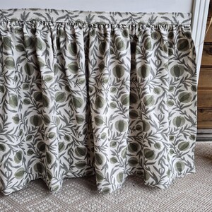 May include: A gathered valance with a botanical pattern. The fabric features a repeating design of green and grey leaves and fruit on a white background. The valance is hanging in front of a wooden wall.