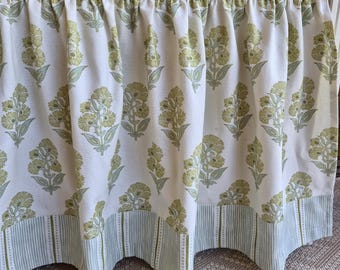 May include: A white fabric valance with a repeating pattern of green floral bouquets. The bottom edge features a green and white striped border. The valance is gathered at the top, creating soft folds.