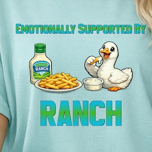 May include: Light blue t-shirt with the text "Emotionally Supported by Ranch." The graphic features a cartoon duck eating a french fry, a bottle of ranch dressing, a plate of fries, and a bowl of ranch.