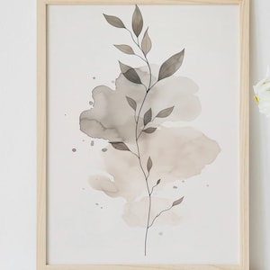 May include: A framed watercolor print featuring a botanical design with a branch and leaves in shades of gray and beige. The artwork is displayed on a white surface, next to a white vase with white flowers.
