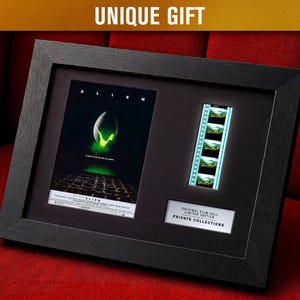 May include: Framed black artwork featuring the movie poster for "Alien" and a strip of film cells. The poster has a green and black color scheme. The text "UNIQUE GIFT" is at the top. The frame includes a white label with text.