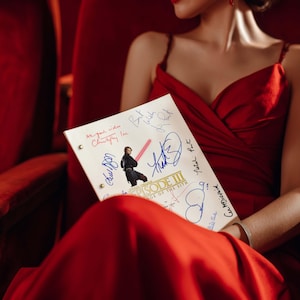 Pode incluir: Um vestido vermelho e um roteiro de Star Wars: Epis&oacute;dio III. O roteiro &eacute; assinado por v&aacute;rias pessoas, incluindo Christopher Lee. A imagem mostra uma pessoa em um vestido vermelho segurando o roteiro.