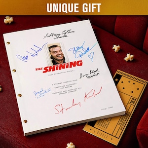Pode incluir: Um roteiro de filme branco para "The Shining" com assinaturas, uma foto de Jack Nicholson e o título do filme em vermelho. Um bilhete de cinema e pipocas estão em uma superfície de veludo vermelho. O texto "UNIQUE GIFT" está no topo.