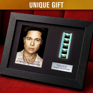 Könnte beinhalten: Schwarzer gerahmter Display mit einem Porträt von Brad Pitt und einem Filmstreifen. Das Porträt stammt aus dem Film "Der seltsame Fall des Benjamin Button". Das Display enthält eine kleine Tafel mit Text.