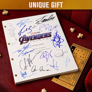 以下が含まれることがあります： 「アベンジャーズ/エンドゲーム」のタイトルと複数の青いインクのサインが入った白い脚本本。「UNIQUE GIFT」の文字が上部にあります。ヴィンテージの映画チケットとポップコーンも表示されています。