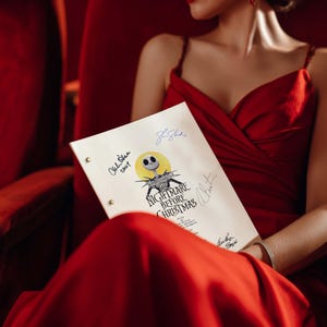 May include: A script for "The Nightmare Before Christmas" with signatures, held by a person wearing a red dress. The script features the film's title and a graphic of Jack Skellington. The background is a red theater seat.