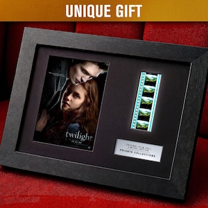 Pode incluir: Uma moldura preta contendo um pôster do filme Crepúsculo, uma tira de filme e uma placa com texto. A moldura está sobre uma superfície vermelha. O texto "UNIQUE GIFT" está no topo. A tira de filme mostra uma série de imagens.