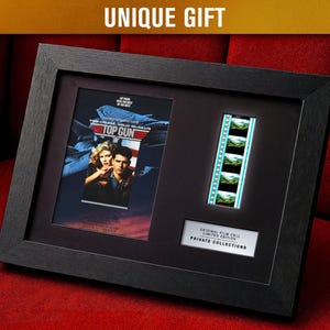 May include: Framed Top Gun movie memorabilia. The black frame holds a movie poster and a strip of film. The poster features Tom Cruise and Kelly McGillis. The film strip shows several frames. The text "UNIQUE GIFT" is at the top.