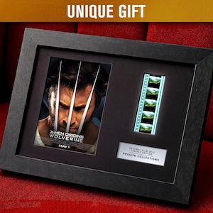 May include: Framed X-Men Origins: Wolverine film memorabilia. The black frame contains a movie poster image and a strip of film cells. The text "UNIQUE GIFT" is at the top. The frame is on a red surface.