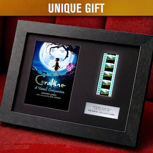 Può includere: Opera d'arte incorniciata in nero con una cella cinematografica e una copertina del libro di "Coraline: A Visual Companion". La copertina mostra una ragazza che cammina verso una luna. La cornice ha il testo "UNIQUE GIFT" in alto.
