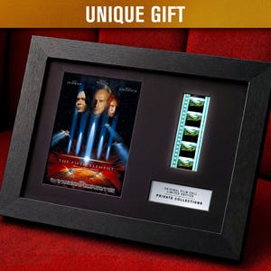 May include: Framed movie memorabilia featuring a film poster and a strip of film cells from "The Fifth Element." The black frame holds the poster with actors' faces and the film strip. The text "UNIQUE GIFT" is at the top.