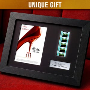 May include: Black framed artwork with a movie poster for "The Devil Wears Prada" and film cells. The poster shows a red high heel. The frame is black, and the text "UNIQUE GIFT" is at the top.