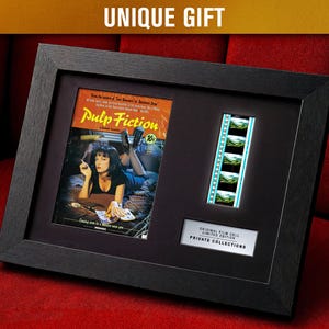 May include: Framed Pulp Fiction movie poster print with a film strip and text "UNIQUE GIFT". The poster features a woman smoking a cigarette. The frame is black and sits on a red surface.