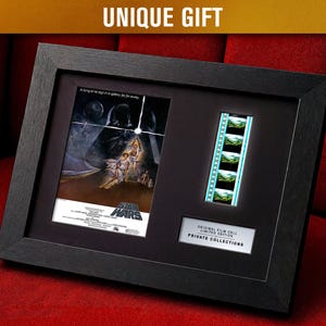 May include: Framed Star Wars movie poster and film cell. The black frame holds the movie poster and a strip of film. The poster features Darth Vader and Luke Skywalker. The text "UNIQUE GIFT" is at the top.