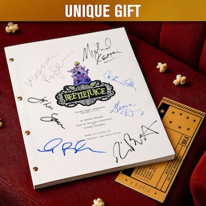 May include: A white script with signatures, the title "Beetlejuice", and a movie ticket are on a red velvet surface. The script has gold-colored binding and is surrounded by popcorn. The text "UNIQUE GIFT" is at the top.