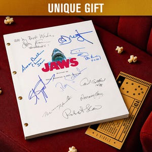 Op de afbeelding: Een wit script met handtekeningen en het woord "JAWS" in rood en blauw, met een haai-afbeelding. De tekst "UNIQUE GIFT" staat bovenaan. Een bioscoopkaartje en popcorn zijn ook zichtbaar.
