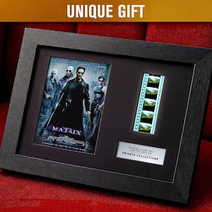 May include: Black framed display with a movie poster and film strip from "The Matrix." The poster shows the main characters. The film strip has several frames. The text "UNIQUE GIFT" is at the top.