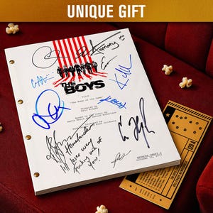 May include: A white script with signatures, the title "The Boys", and the text "UNIQUE GIFT" is displayed on a red surface. A movie ticket and popcorn are also visible. The script has brass fasteners.