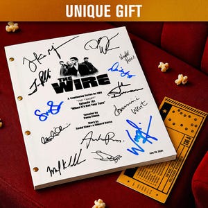 Puede incluir: Un guion blanco de "The Wire", episodio "The Target", con múltiples firmas, ojales dorados y una entrada de cine. El guion está sobre una superficie de terciopelo rojo con palomitas de maíz esparcidas.