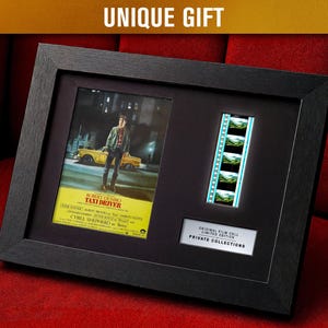 Könnte beinhalten: Schwarzer gerahmter Kunstdruck mit einem Filmausschnitt und einem Filmplakat von "Taxi Driver". Das Plakat zeigt einen Mann vor einem gelben Taxi. Der Text "UNIQUE GIFT" steht oben.