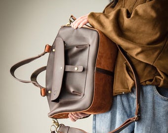 Pode incluir: Uma mala de mão em couro castanho escuro com um bolso frontal liso com fecho de aba, ferragens em tom de latão e um pendente em couro em forma de coração removível. A mala inclui uma alça de ombro longa ajustável e duas alças curtas.