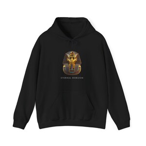 Peut inclure: Un sweat-shirt à capuche noir avec un motif central représentant un masque de pharaon égyptien doré aux accents bleus et rouges. Sous le masque, le texte ETERNAL HORIZON est imprimé en lettres capitales blanches. Manches longues.