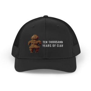Peut inclure: Une casquette trucker noire avec un dos en filet et un panneau avant solide. L'avant présente un graphique de figurine en argile brune texturée à gauche du texte en lettres capitales blanches qui indique : TEN THOUSAND YEARS OF CLAY.