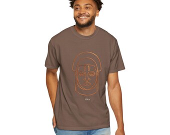 Puede incluir: Una camiseta marrón de manga corta con una ilustración de líneas de color cobre de un rostro con un tocado tradicional centrada en el pecho. Debajo de la ilustración, la palabra IDIA está impresa en letras pequeñas, blancas y mayúsculas.