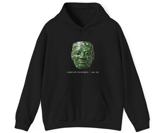 May include: A black hooded sweatshirt featuring a graphic of a green mosaic mask on the chest. Below the mask, the text reads LORD OF PALENQUE // 683 AD. The garment includes a drawstring hood, long sleeves, and a front kangaroo pocket.