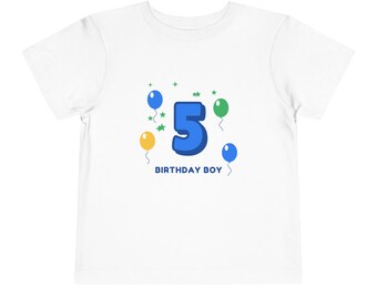 Könnte beinhalten: Ein weißes Kurzarm-T-Shirt mit einer Grafik einer großen blauen Zahl 5, umgeben von kleinen grünen Sternen sowie gelben, blauen und grünen Luftballons. Unter der Zahl steht der Text BIRTHDAY BOY in blauen Großbuchstaben.