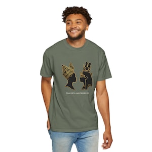 May include: An olive green short-sleeve t-shirt featuring a graphic print of two black and gold silhouettes of ancient figures facing each other. Below the silhouettes, the text reads TIMELESS MATRIARCHS in a clean, white, sans-serif font.