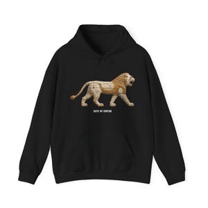 May include: A black hooded sweatshirt featuring a graphic of a walking lion with a textured, tan-colored body and a darker mane. Below the lion, the text GATE OF ISHTAR is printed in white capital letters. The hoodie has long sleeves and a front pocket.