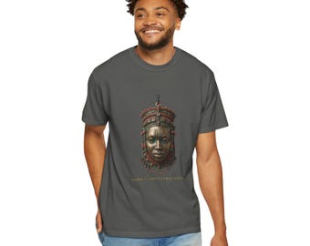 Puede incluir: Una camiseta gris carbón con un gráfico central de una máscara en tonos bronce adornada con cuentas rojas y patrones intrincados. Debajo de la máscara, el texto "YORUBA OF ANCESTRAL GRACE" aparece en letras doradas. Cuello redondo y mangas cortas.