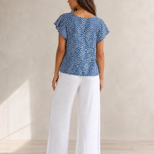 May include: A blue short-sleeved top featuring a white speckled pattern with flutter sleeves and a round neckline, paired with solid white wide-leg trousers. The ensemble consists of a patterned blouse and plain white pants with a loose fit.