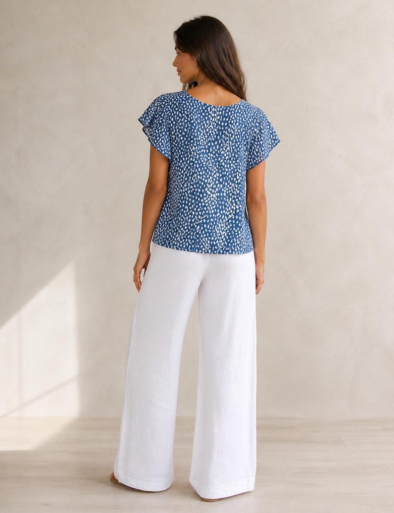 May include: A blue short-sleeved top featuring a white speckled pattern with flutter sleeves and a round neckline, paired with solid white wide-leg trousers. The ensemble consists of a patterned blouse and plain white pants with a loose fit.