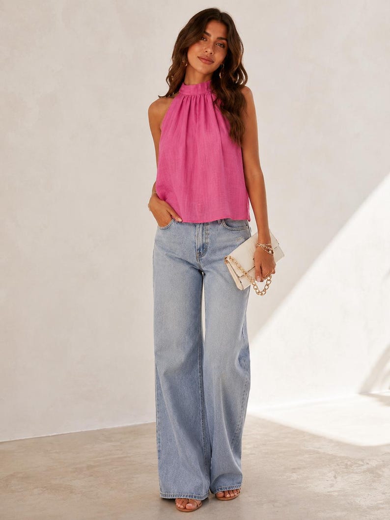 May include: A bright pink sleeveless halter top with a gathered neckline paired with light blue wide-leg denim jeans and a white rectangular clutch bag featuring a gold chain strap. The outfit is completed with open-toe sandals.