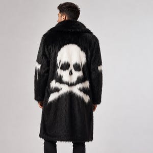 Könnte beinhalten: Schwarzer Kunstfellmantel mit großem weißem Totenkopf- und gekreuzten Knochen-Design auf dem Rücken. Der Mantel hat einen breiten Kragen und lange Ärmel. Das Model trägt eine schwarze Jeans und weiße Turnschuhe. Ein auffälliges Kleidungsstück.