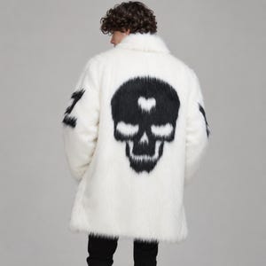 Könnte beinhalten: Ein weißer Kunstpelzmantel mit einer großen schwarzen Totenkopfgrafik auf dem Rücken, die ein kleines Herz auf der Stirn zeigt. Der Mantel hat lange Ärmel mit schwarzen Details an den Oberarmen und einen hohen Kragen, abgebildet von hinten.