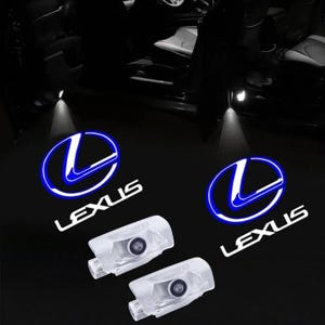 Könnte beinhalten: Autotür-Projektorleuchten, die das Lexus-Logo in Weiß und Blau anzeigen. Die Lichter projizieren das Logo auf den Boden und beleuchten den Bereich in der Nähe der Autotüren. Das Bild zeigt zwei Sätze von Lichtern.