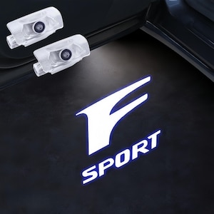 May include: Two clear, rectangular car door lights are positioned above a glowing white logo with the word "SPORT" in blue. The logo is a stylized "F" shape. The lights project onto a dark surface.