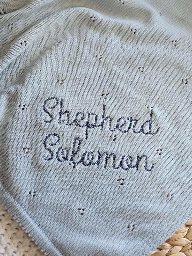 Puede incluir: Una manta de beb&eacute; azul claro con el nombre "Shepherd Solomon" bordado en hilo azul m&aacute;s oscuro. La manta tiene un delicado dise&ntilde;o calado con peque&ntilde;os agujeros espaciados uniformemente.