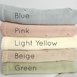 Puede incluir: Una pila de cinco mantas de punto en varios colores: azul, rosa, amarillo claro, beige y verde. Cada manta tiene un borde enrollado y un patr&oacute;n de punto texturizado. El color de cada manta est&aacute; etiquetado con texto.