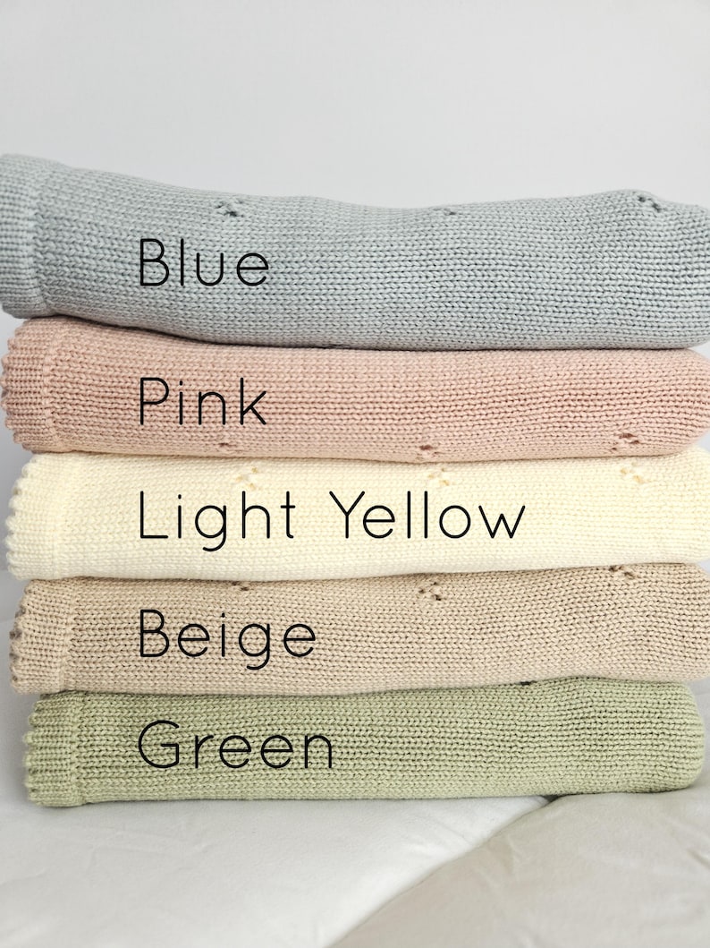 Puede incluir: Una pila de cinco mantas de punto en varios colores: azul, rosa, amarillo claro, beige y verde. Cada manta tiene un borde enrollado y un patr&oacute;n de punto texturizado. El color de cada manta est&aacute; etiquetado con texto.