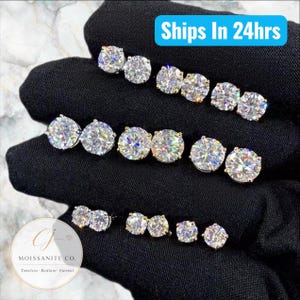 May include: Three rows of round-cut moissanite stud earrings arranged by size, from largest to smallest, displayed on a black fabric background. The text "Ships In 24hrs" appears in a blue box, and a circular logo reads "CJ MOISSANITE CO."