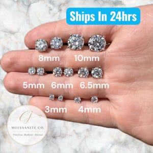 May include: A variety of moissanite stud earrings in different sizes, ranging from 3mm to 10mm, are displayed. The earrings are round-cut and set in a silver-colored metal. The image includes the text "Ships In 24hrs" and the logo for "Moissanite Co."