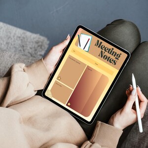 May include: A digital tablet displaying a "Meeting Notes" template. The template features sections for notes, agenda, and dates, with a color scheme of tan, brown, and gold. A stylus rests near the tablet, suggesting note-taking. The tablet is held in a person's lap.