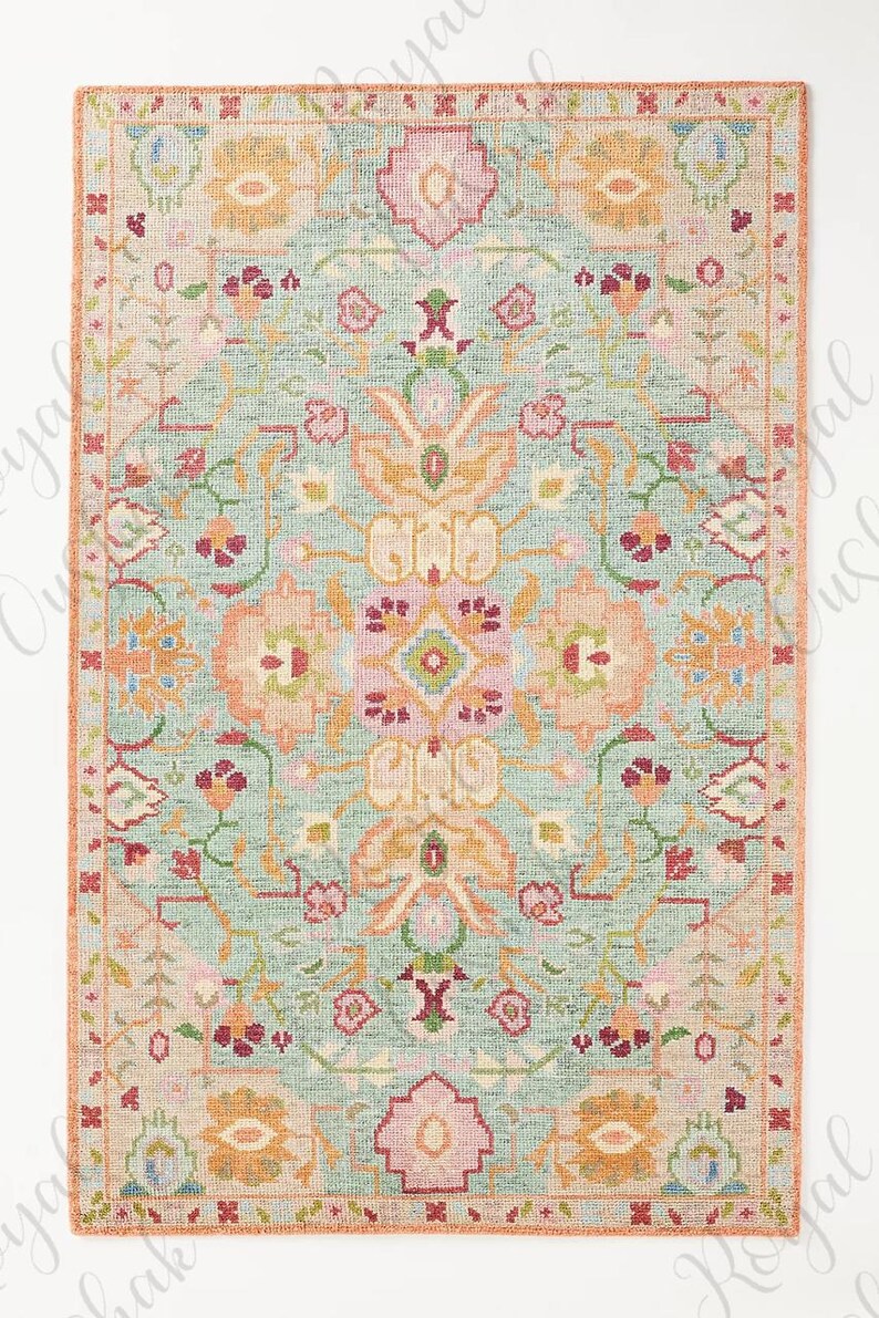 May include: A rectangular rug with a light blue background and a floral pattern in shades of pink, orange, and green. The rug has a border in a similar color palette. The design is symmetrical and features stylized flowers and leaves.